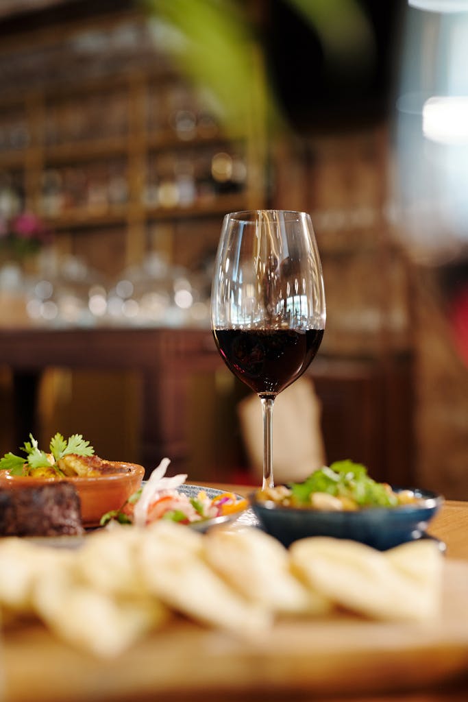 Close-up of a glass of red wine with ceramic bowls and a vegetable salad on a restaurant table.