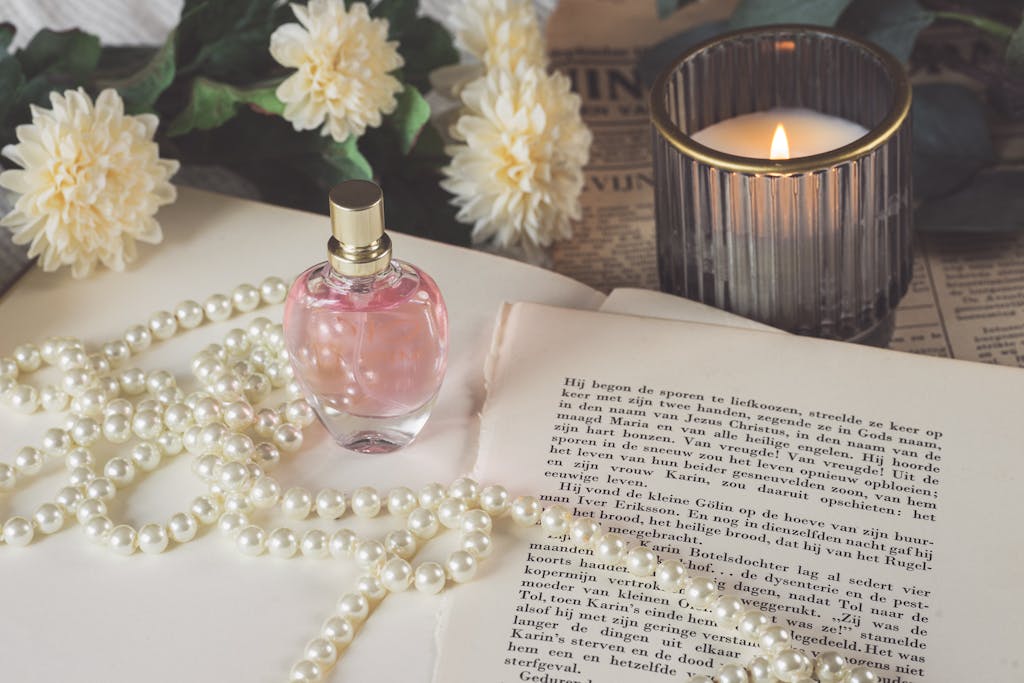 A sophisticated still life featuring a perfume bottle, pearls, and a candle set on vintage papers.